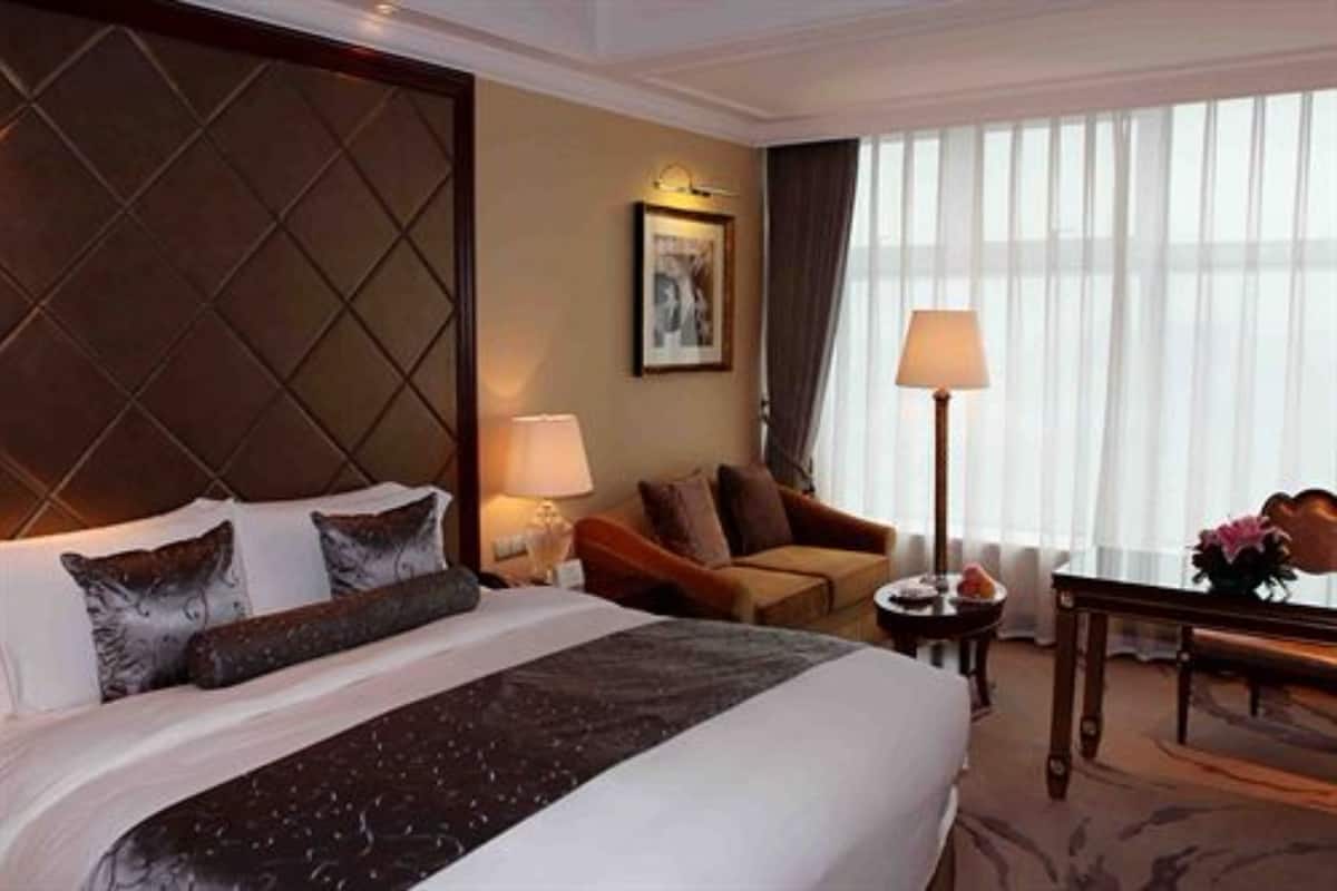 Ett hotellrum med en stor säng, en sittgrupp med soffa och fåtölj, ett litet bord med en lampa och ett fönster med tunna, genomskinliga gardiner.