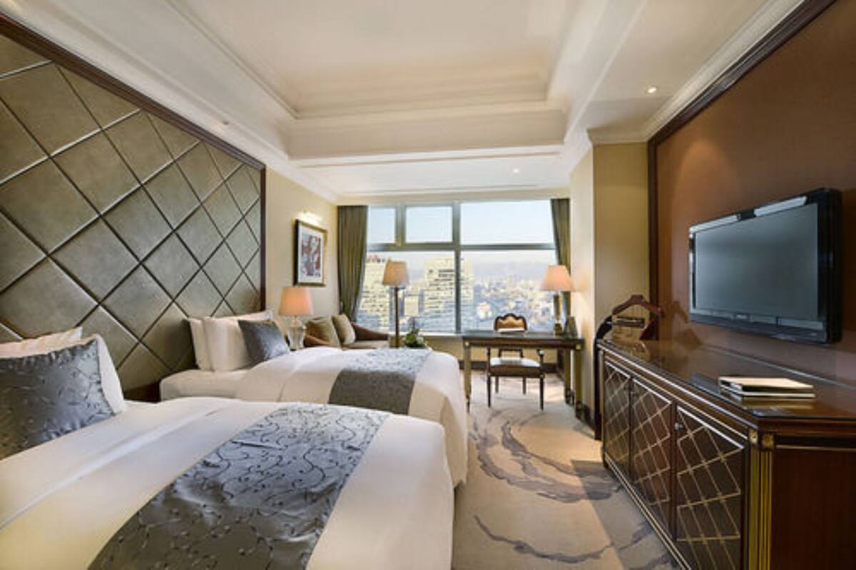 Ett hotellrum med två sängar, ett skrivbord, en tv och ett stort fönster med utsikt över staden.