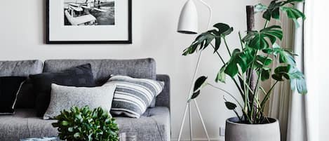 A living room with a grey sofa, a coffee table with a plant and a book, a floor lamp, and a framed picture on the wall.