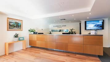 A reception area with a wooden reception desk, a mounted television, and a framed landscape painting on the wall.
