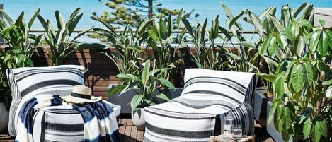 Une terrasse avec deux chaises longues à rayures, une petite table sur laquelle est posé un magazine et une plante en pot.