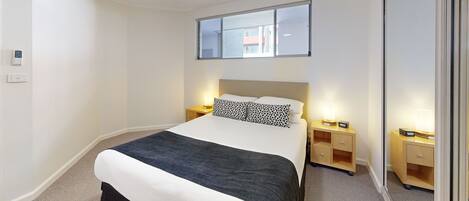 A hotel room with a bed, bedside tables, a ceiling fan, and a window with a view of buildings.