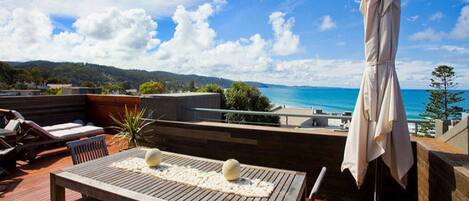 A wooden deck with a table and chairs, an umbrella, and a view of the sea.