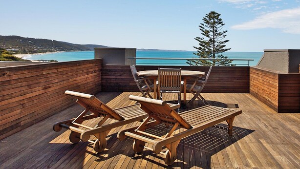 Um deck de madeira com mesa e cadeiras, com vista para a praia e o oceano.