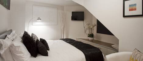 A modern bedroom with a bed, a desk, and a chair. There is a TV mounted on the wall and a plant on the desk.