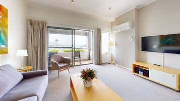 A modern hotel room with a sofa, a chair, a TV, and a balcony with a view.