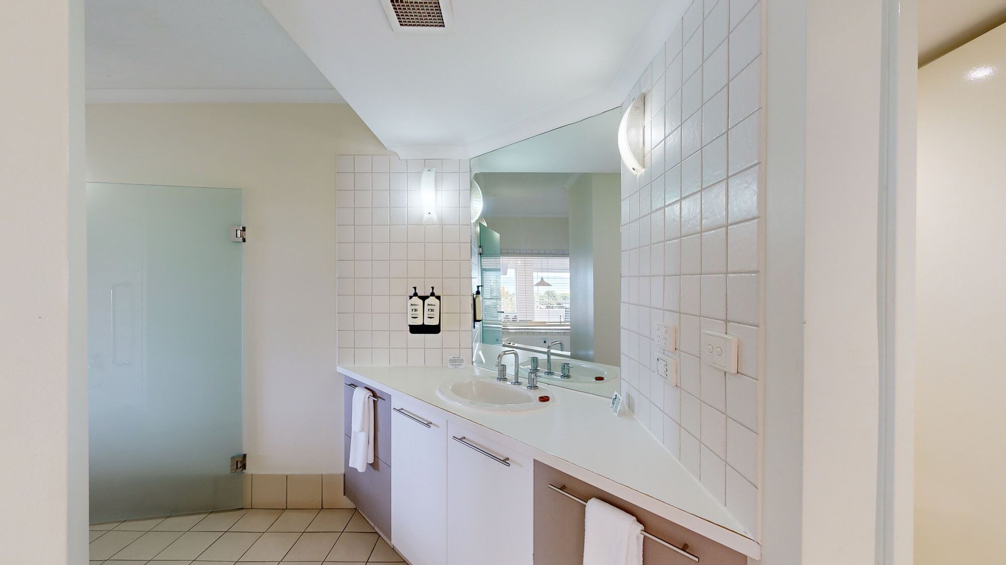 A modern bathroom with a large mirror, white tiles, a sink, and a toilet.