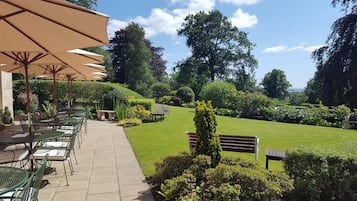An outdoor patio area with tables and chairs, surrounded by well-maintained lawns and trees.