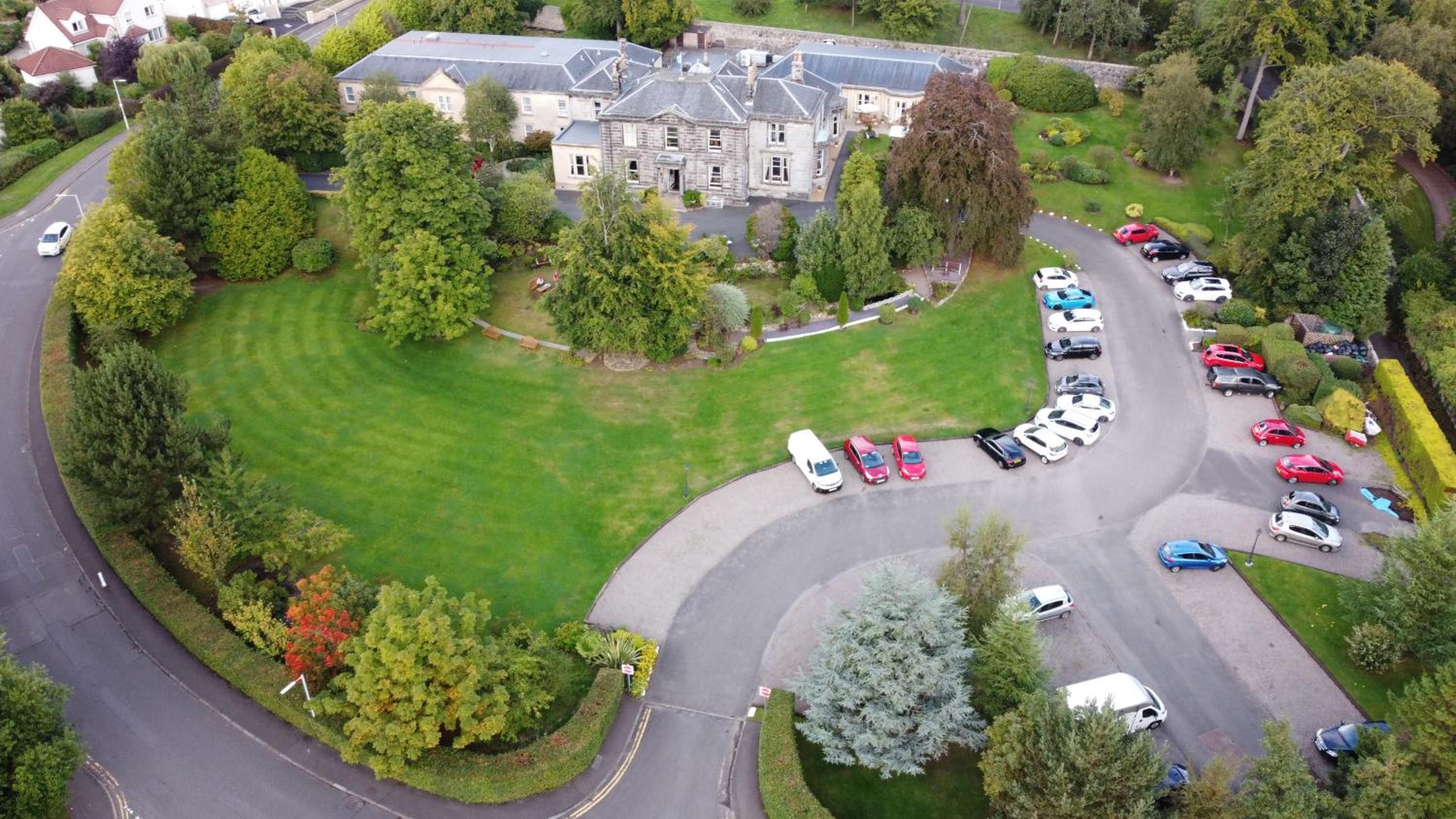 An aerial view of a residential area with a large stone building, a well-maintained lawn, and a parking lot with multiple cars.