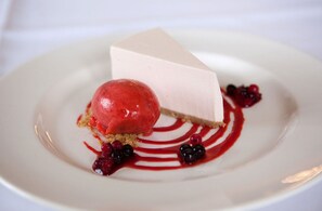 A dessert with a slice of cheesecake and a scoop of red berry ice cream on a white plate with red sauce and berries. - Garvock House Hotel (Dunfermline)