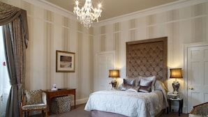 Une chambre à coucher avec un grand lit, deux lampes de chevet, un lustre, un bureau, une chaise et un tableau encadré au mur.
