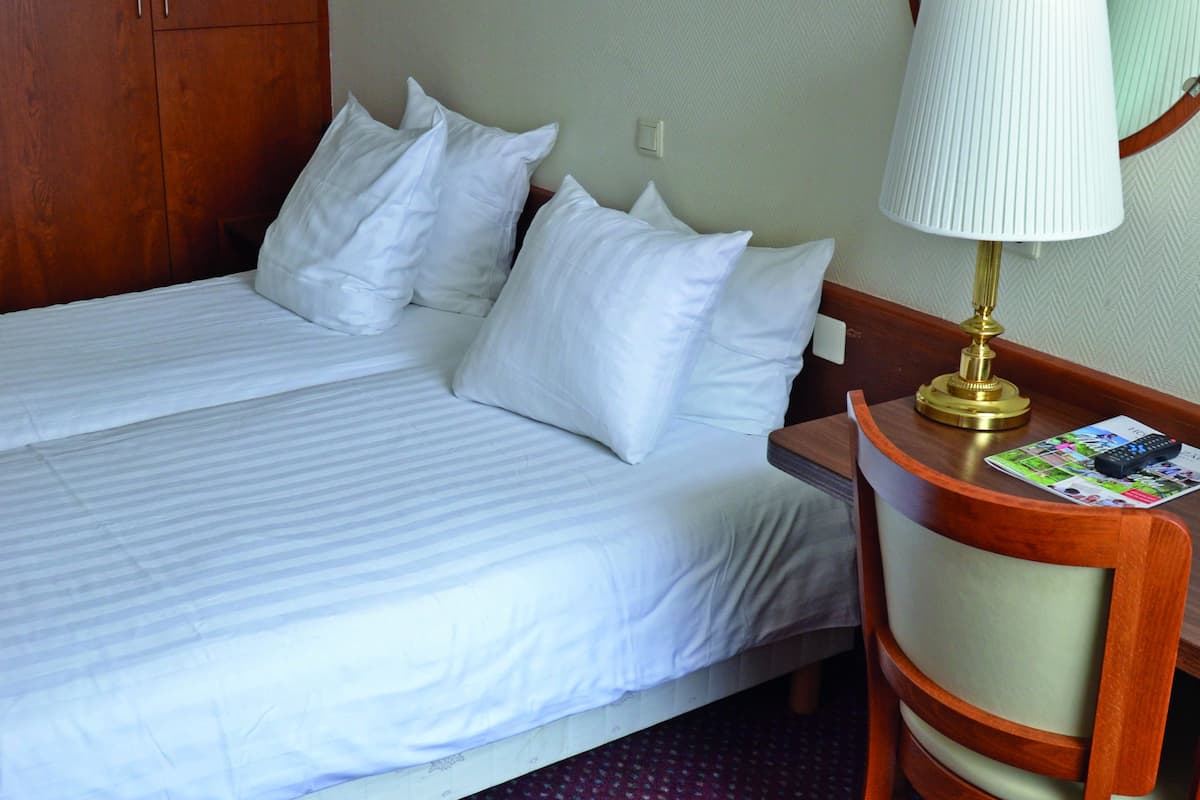 Een hotelkamer met een bed, een bureau met lamp, een stoel en een spiegel.