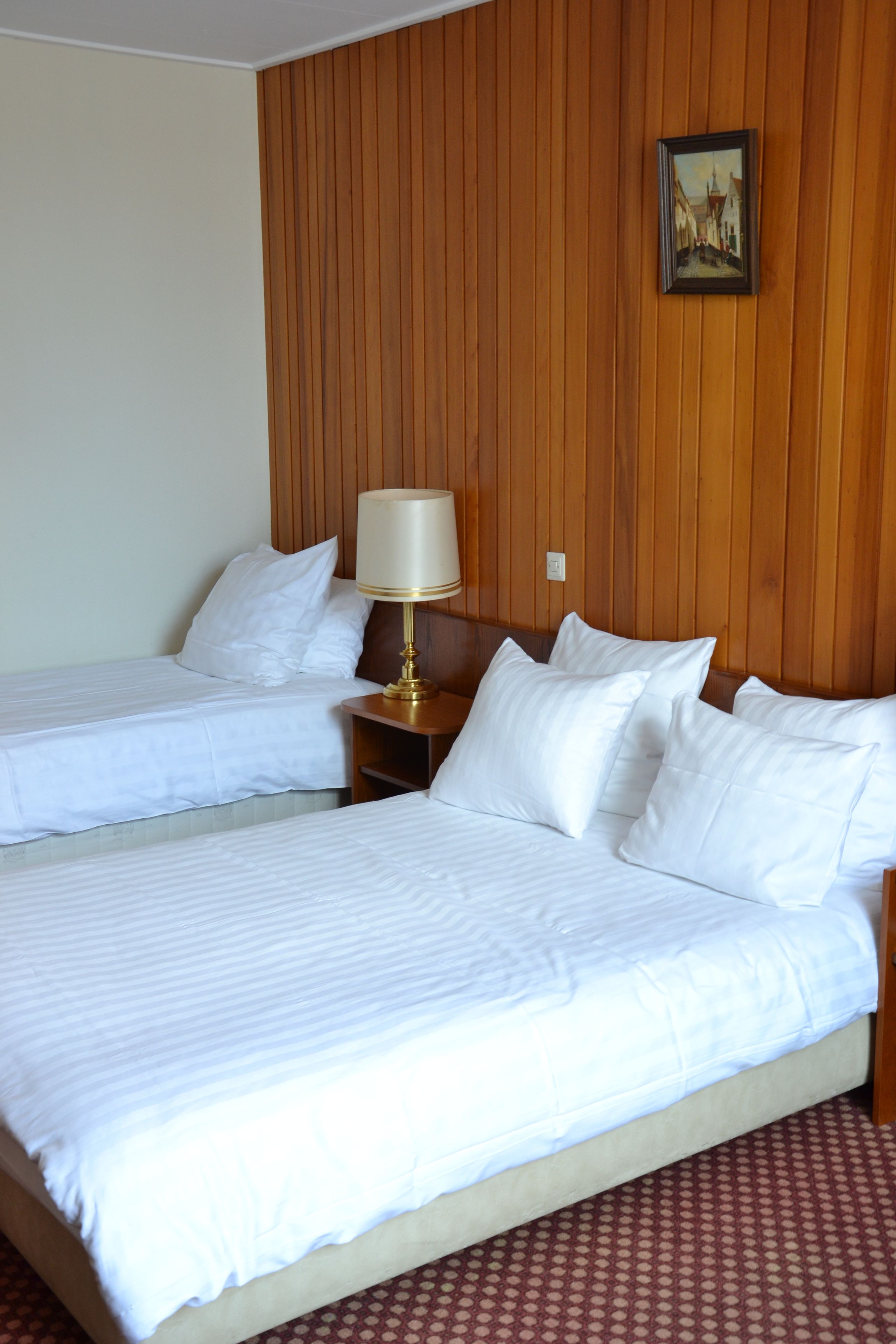 A hotel room with two beds, wooden paneling on the walls, a framed picture, and a nightstand with a lamp.