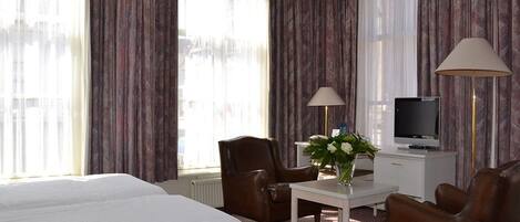 A hotel room with a bed, two chairs, a desk, a TV, and curtains.