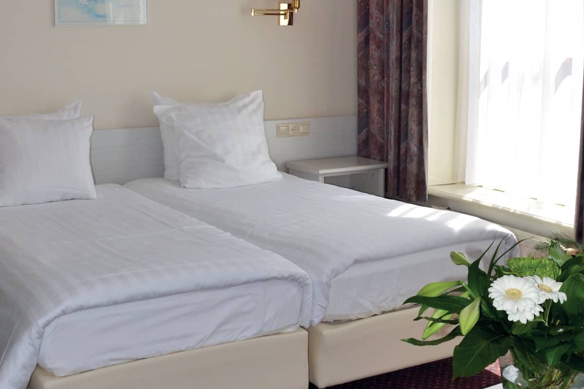 Hotelkamer met twee bedden, een bureau, een stoel, een lamp, een raam met gordijnen en een vaas met bloemen.