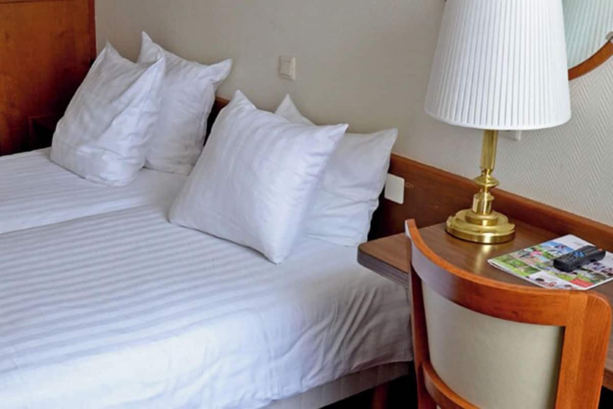 Een hotelkamer met een bed, kussens, een nachtkastje met een lamp en een tijdschrift.