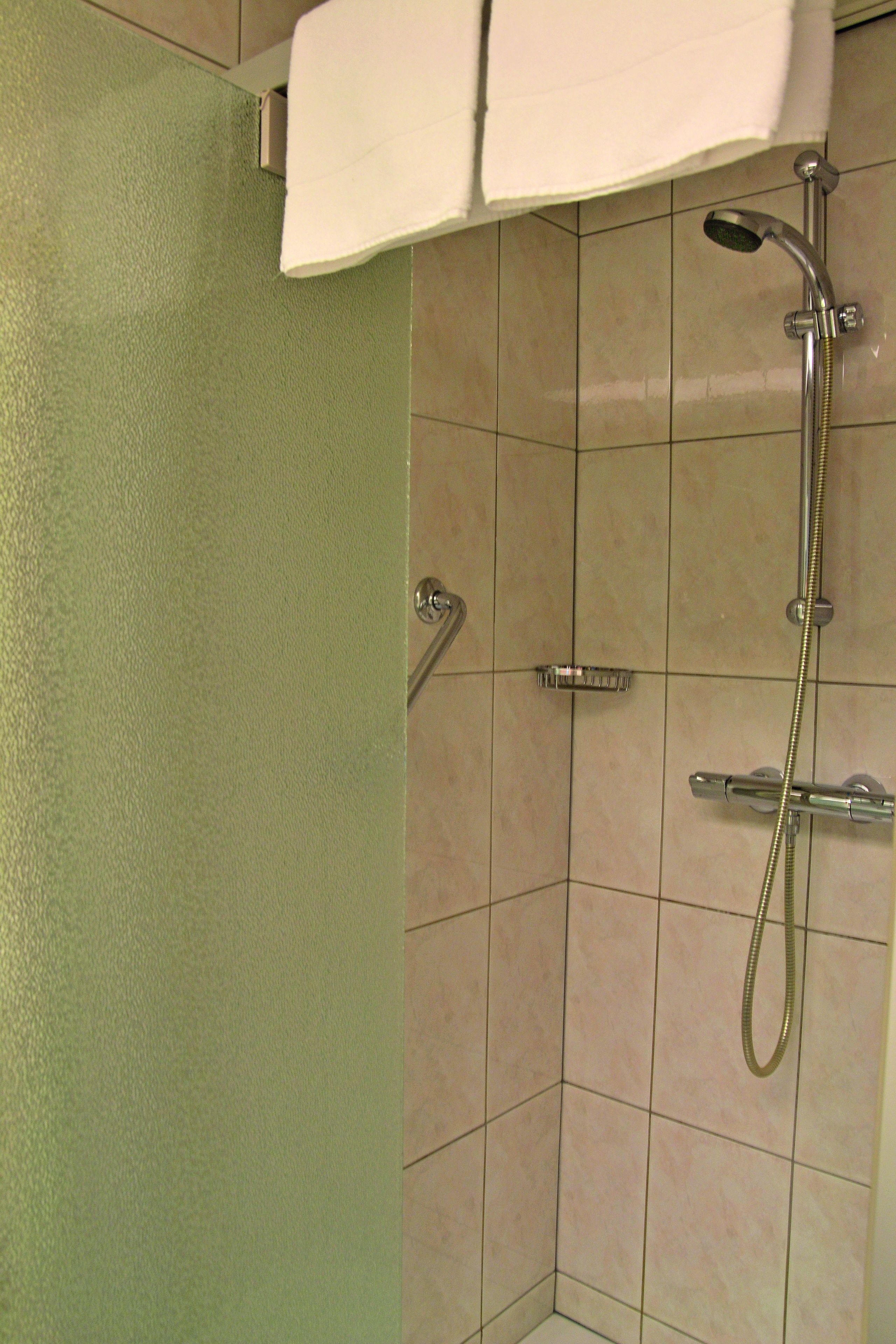 A corner of a bathroom with a shower, a towel hanging on the wall, and a door.