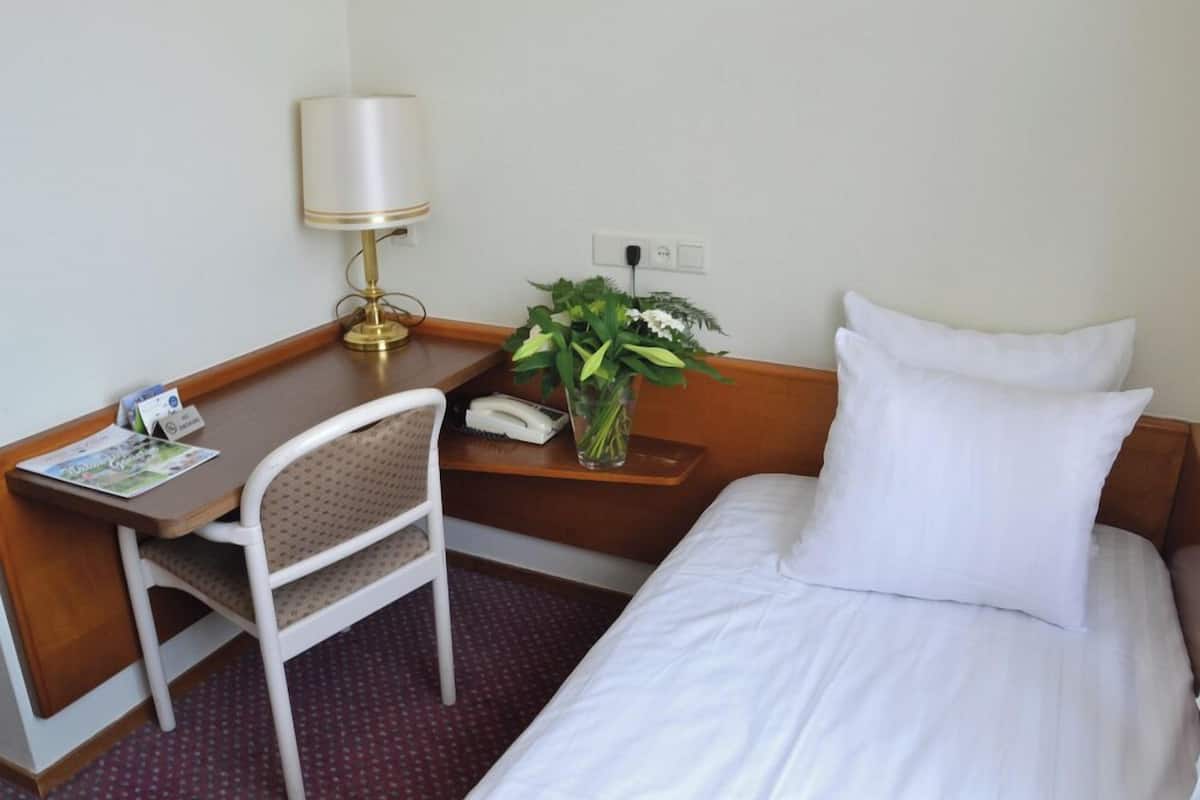 Hotelkamer met een bed, bureau, stoel, lamp, vaas met bloemen en telefoon.