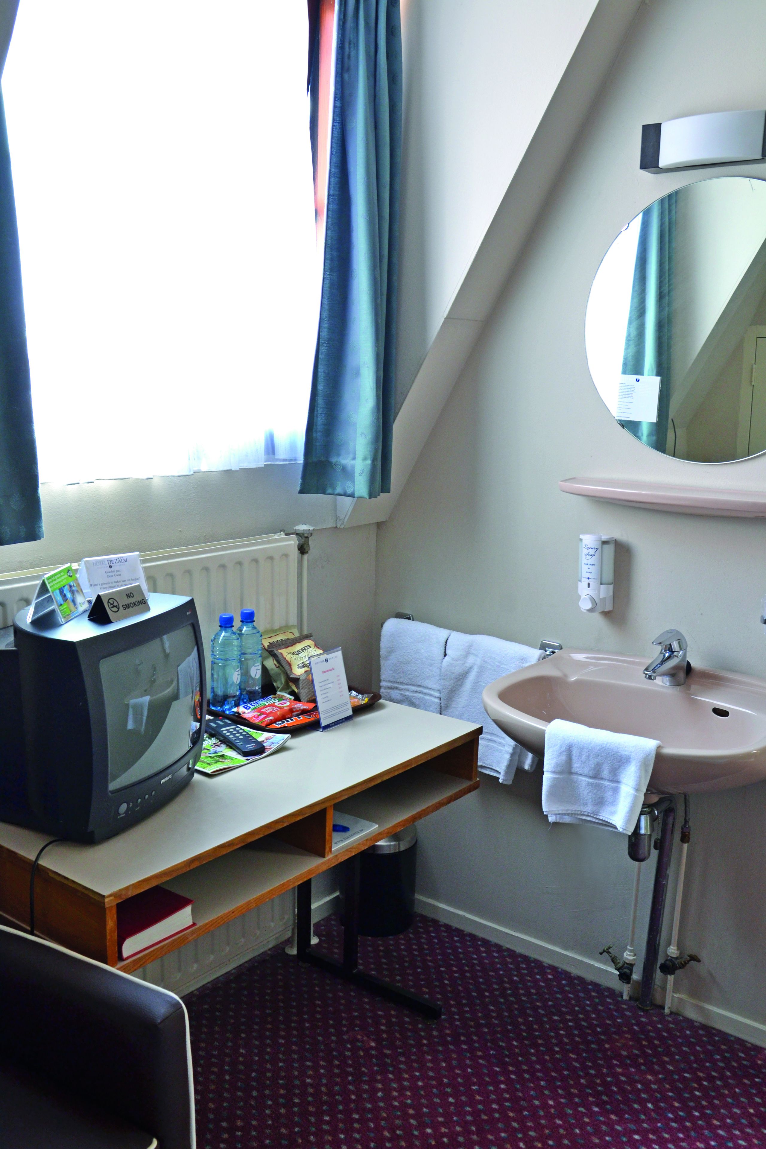 Una habitación de hotel con televisión, lavamanos, espejo y ventana con cortinas.