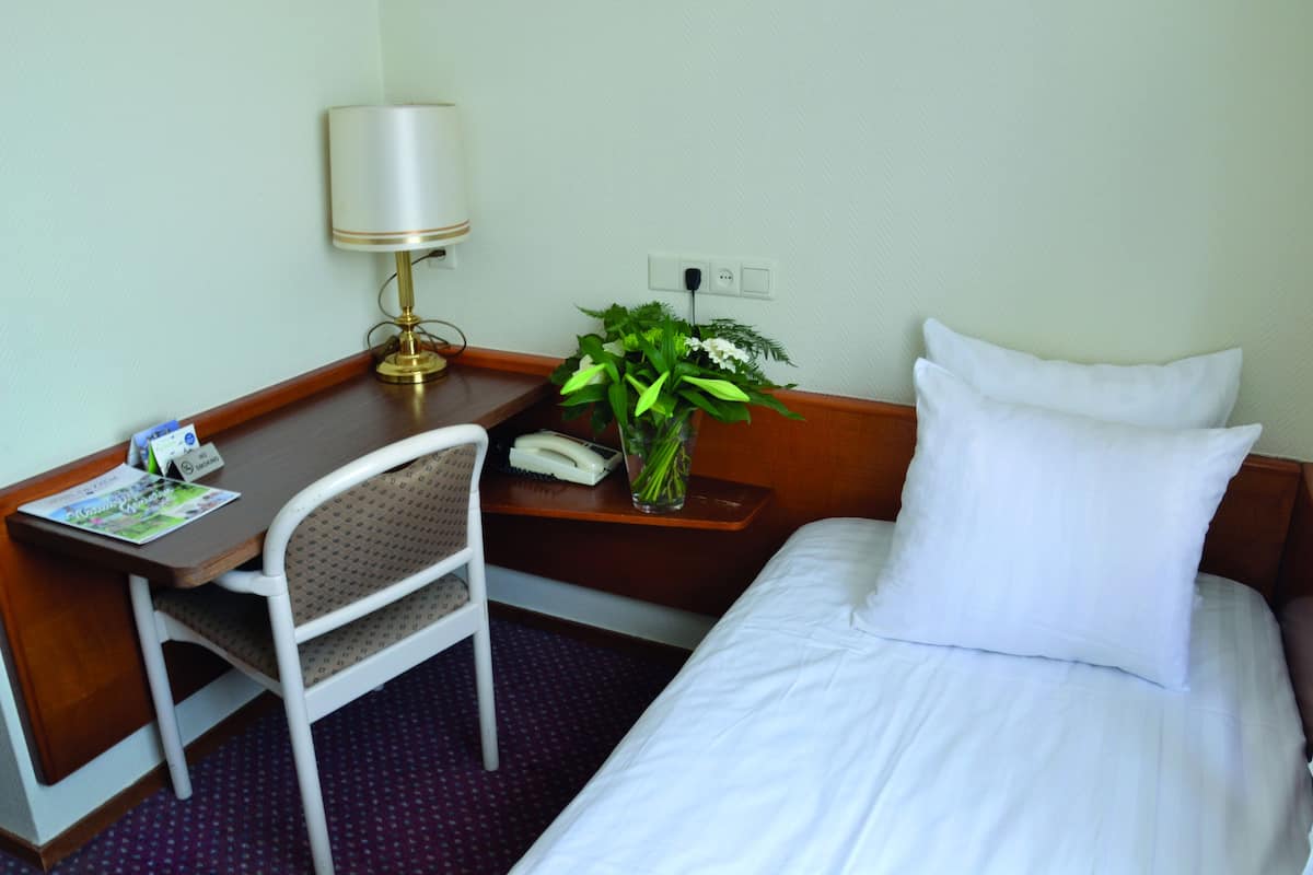 Een hotelkamer met een bed, een bureau, een stoel, een lamp, een vaas met bloemen en een telefoon.