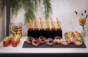 Une variété de hors-d'œuvre présentés sur un plateau, notamment des crevettes, des fraises et d'autres petites portions.