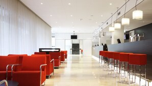 A modern hotel lobby with red seating, a reception desk, and a staircase in the background. - NH Amsterdam Zuid (Amsterdam)