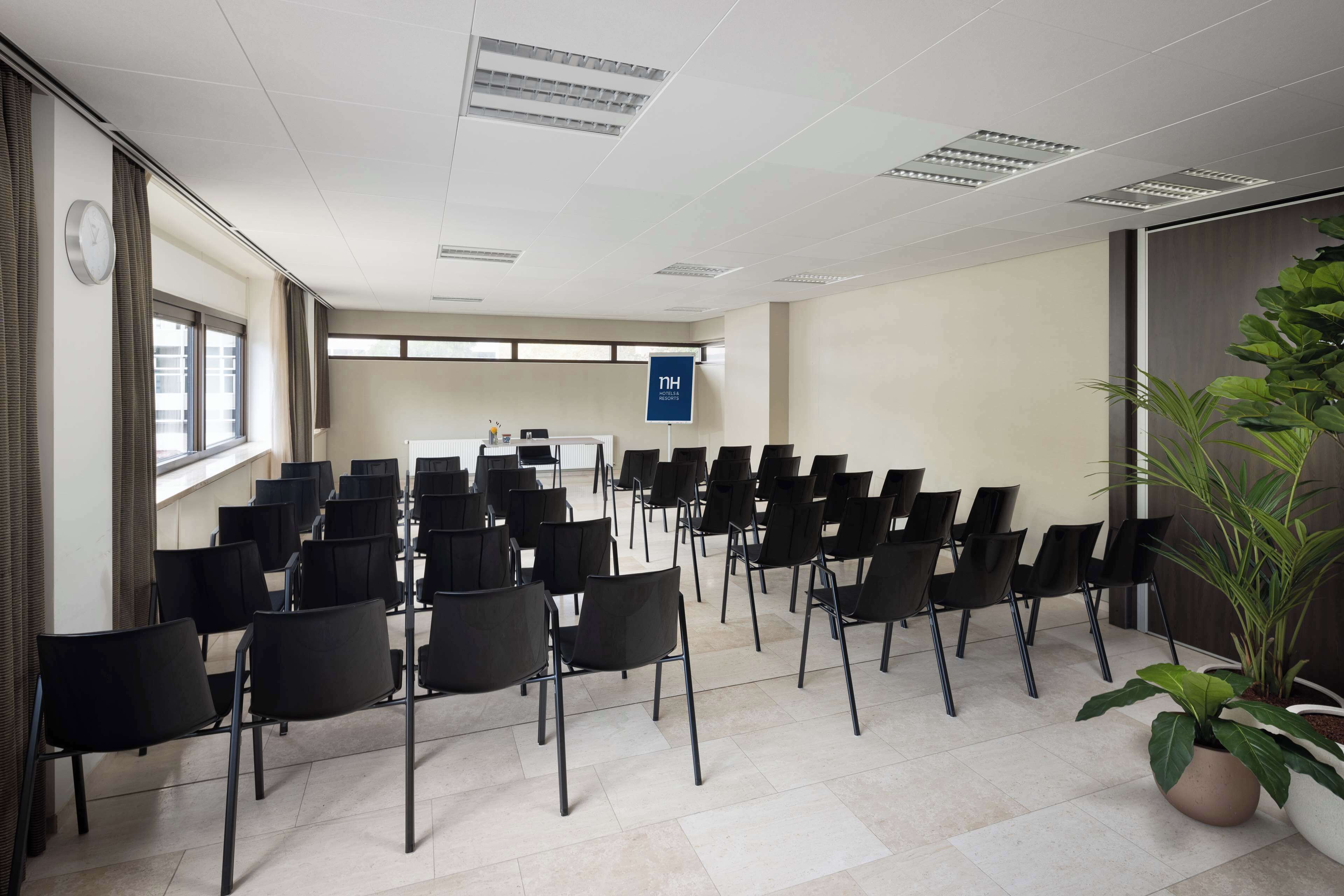 A conference room with rows of black chairs, a clock on the wall, and a sign indicating the room's purpose.