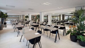 A spacious conference room with multiple tables and chairs, large windows, and potted plants. - NH Amsterdam Zuid (Amsterdam)