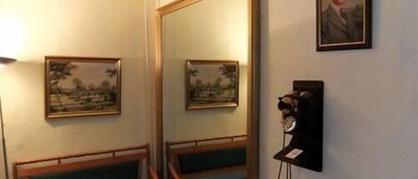 A room with a large mirror, two framed pictures, a telephone, and a bench.