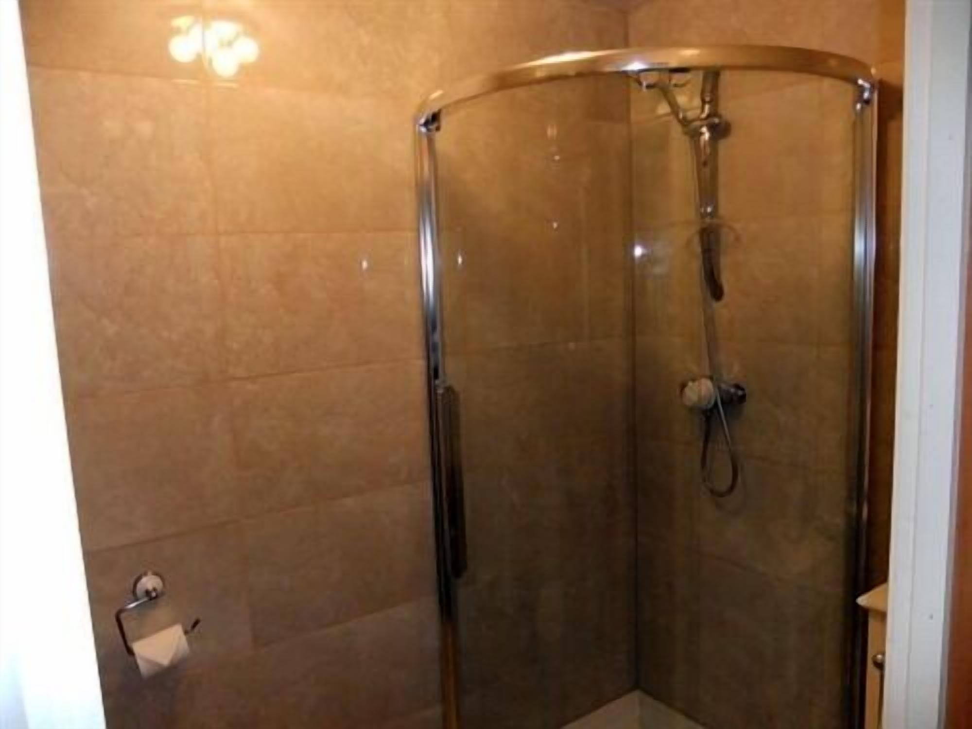 Ducha con mampara de vidrio y puerta curva, cabezal de ducha de mano y grifo instalado en la pared.