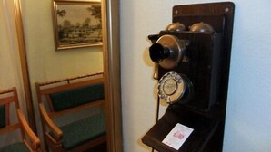 Un teléfono antiguo sujeto a una pared en una habitación con sillas de madera y un cuadro enmarcado.
