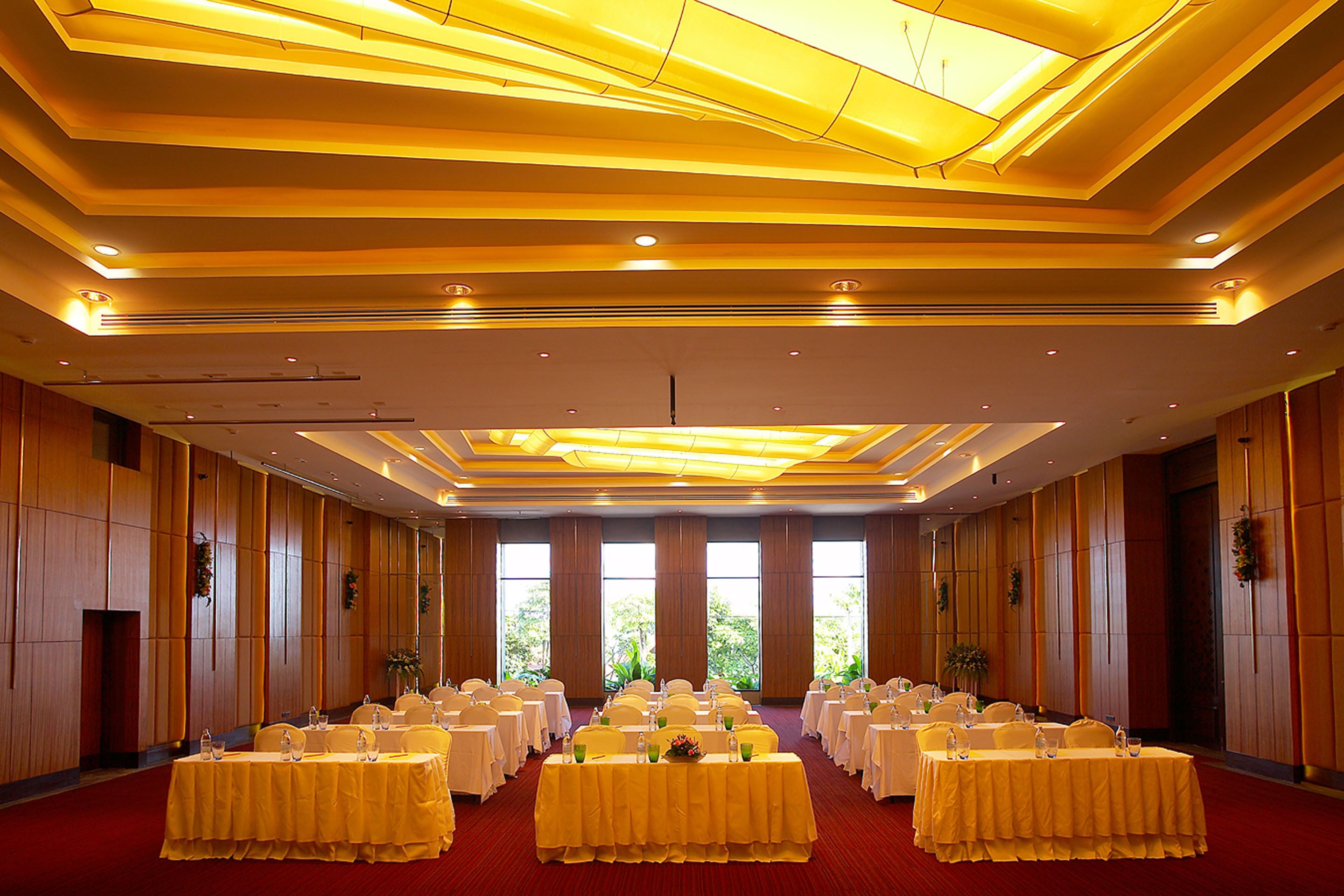 A conference room with rows of tables, chairs, and a large window with a view of greenery.