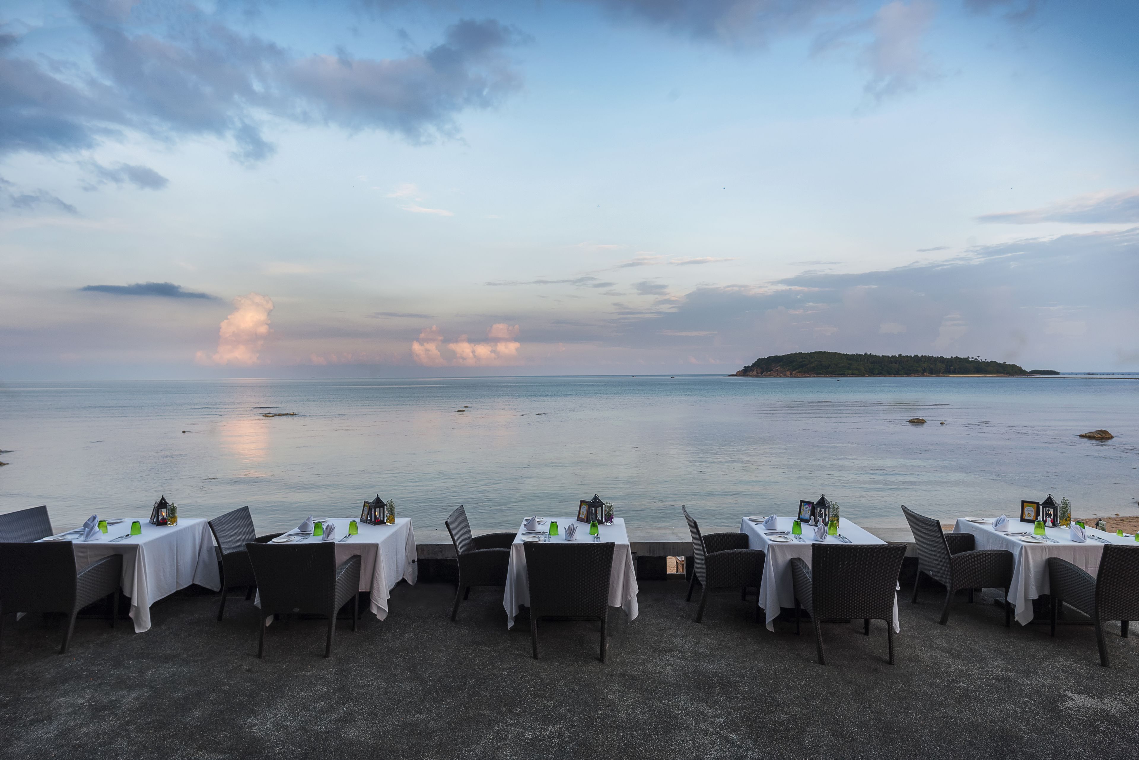 A seaside restaurant with tables set for dining, overlooking the ocean and a distant island.