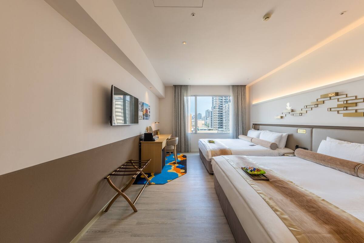 Een hotelkamer met twee bedden, een bureau, een televisie en uitzicht op de stad.