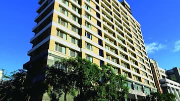 Um hotel alto com vários andares, design moderno e céu azul claro ao fundo.