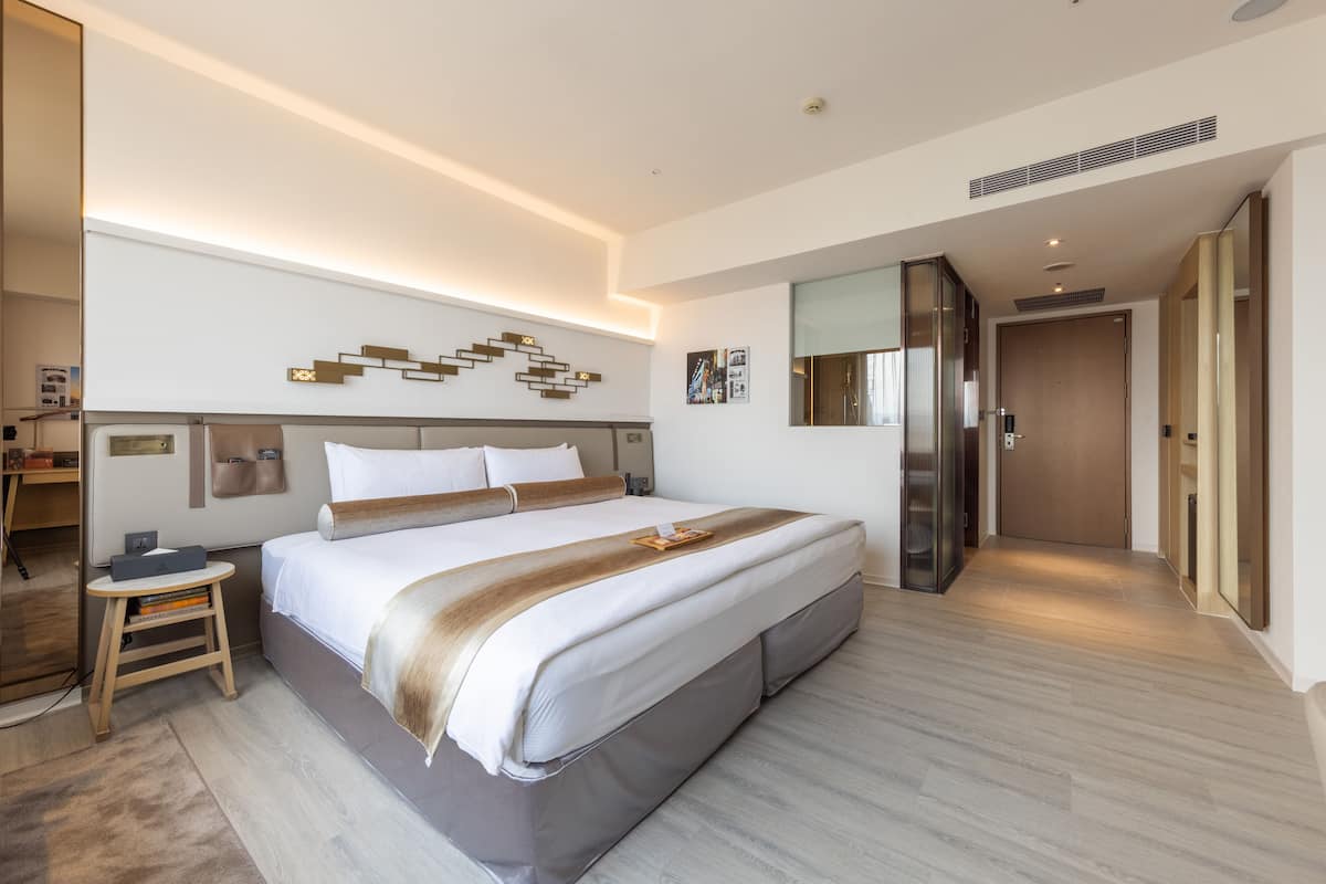 Een moderne hotelkamer met een groot bed, nachtkastjes, een bureau en een spiegel.