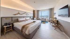Moderni hotellihuone, jossa on suuri sänky, työpöytä, tuoli ja näkymä kaupunkiin.