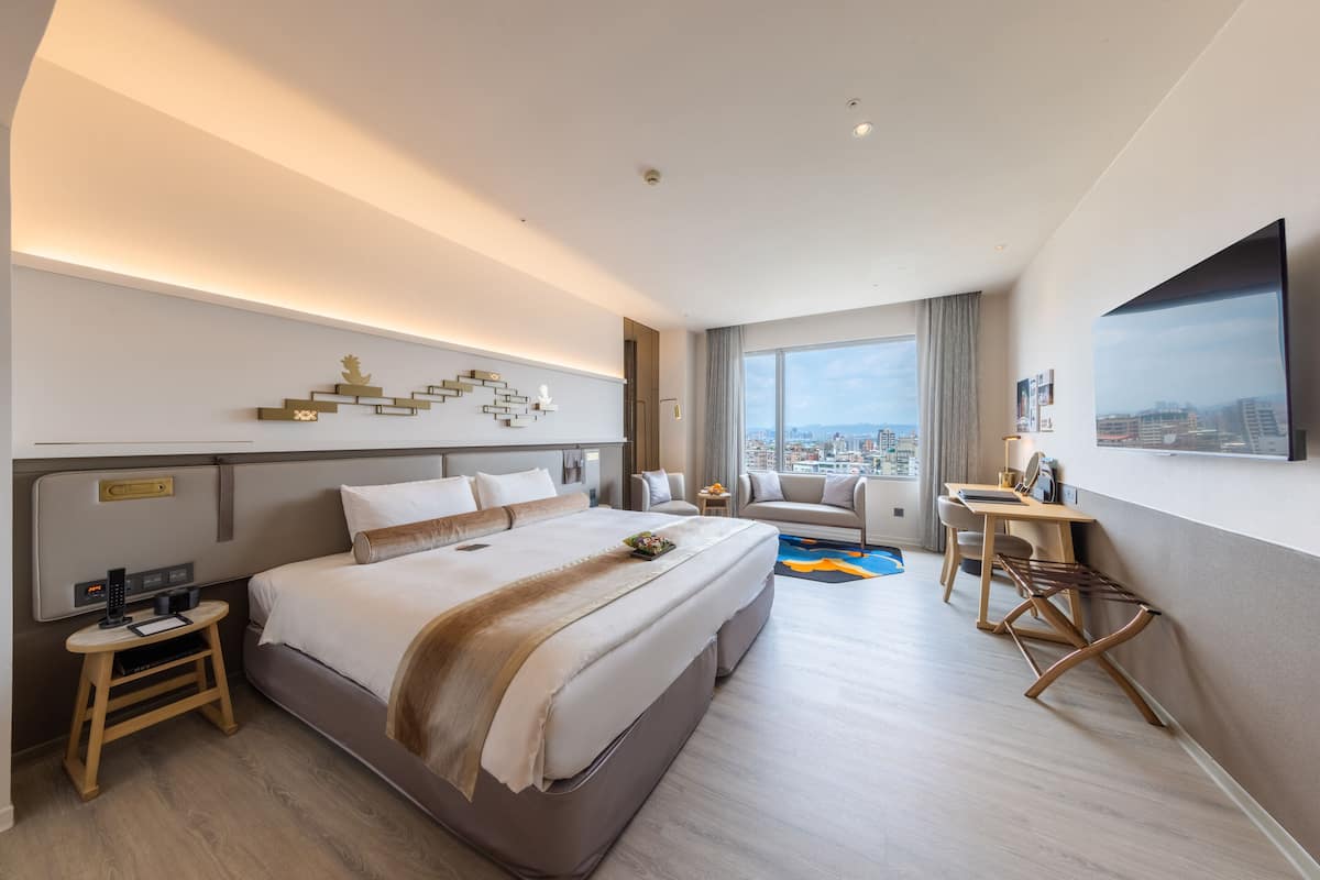 Een moderne hotelkamer met een groot bed, een bureau, een stoel en uitzicht op de stad.