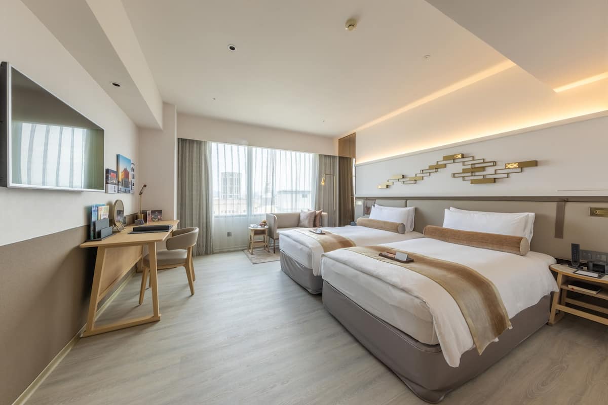 Een hotelkamer met twee bedden, een bureau, een stoel en een groot raam.