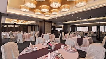 A banquet hall with round tables set for dining, equipped with tablecloths, chairs, and centerpieces.