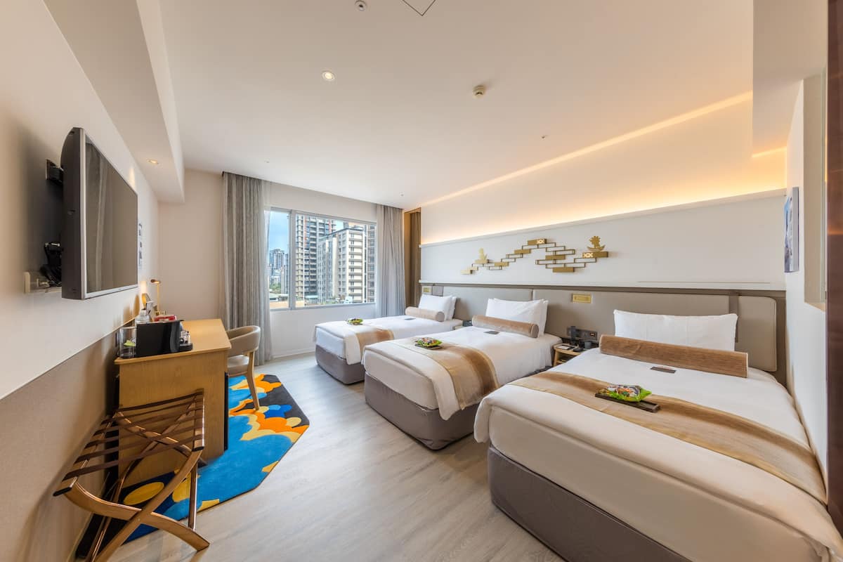 Een moderne hotelkamer met twee bedden, een bureau, een televisie en een groot raam met uitzicht op de stad.