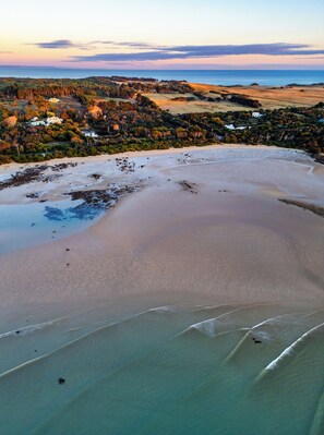 A coastal landscape with a sandy beach and a view of a residential area with houses and trees. - Hawley House (Hawley Beach)
