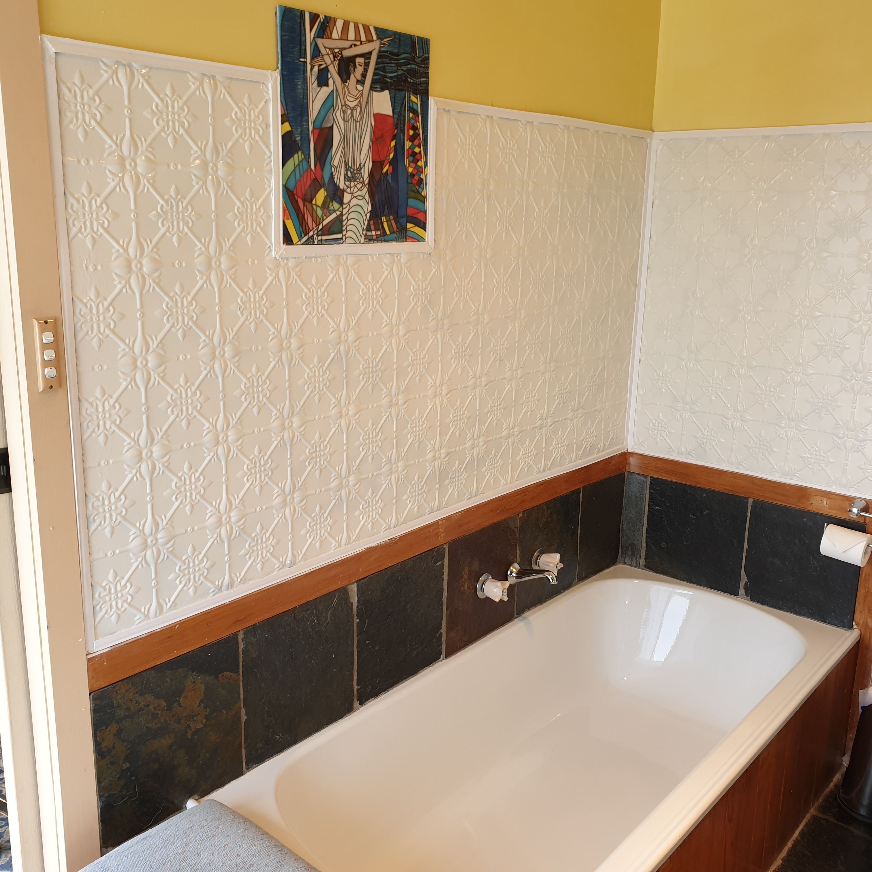 Une salle de bain avec une baignoire blanche, un meuble-lavabo en bois et un panneau décoratif mural.