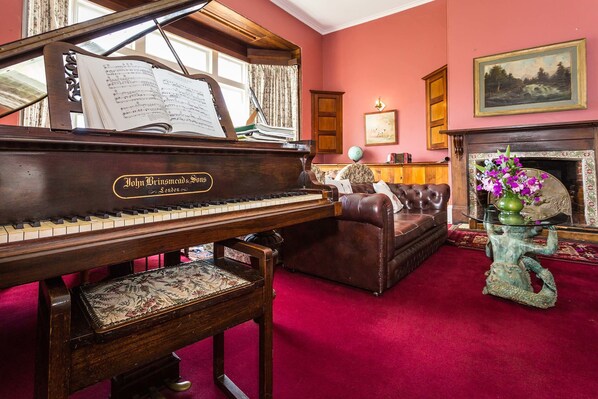 A grand piano with sheet music, a leather sofa, a fireplace, and a painting on the wall.