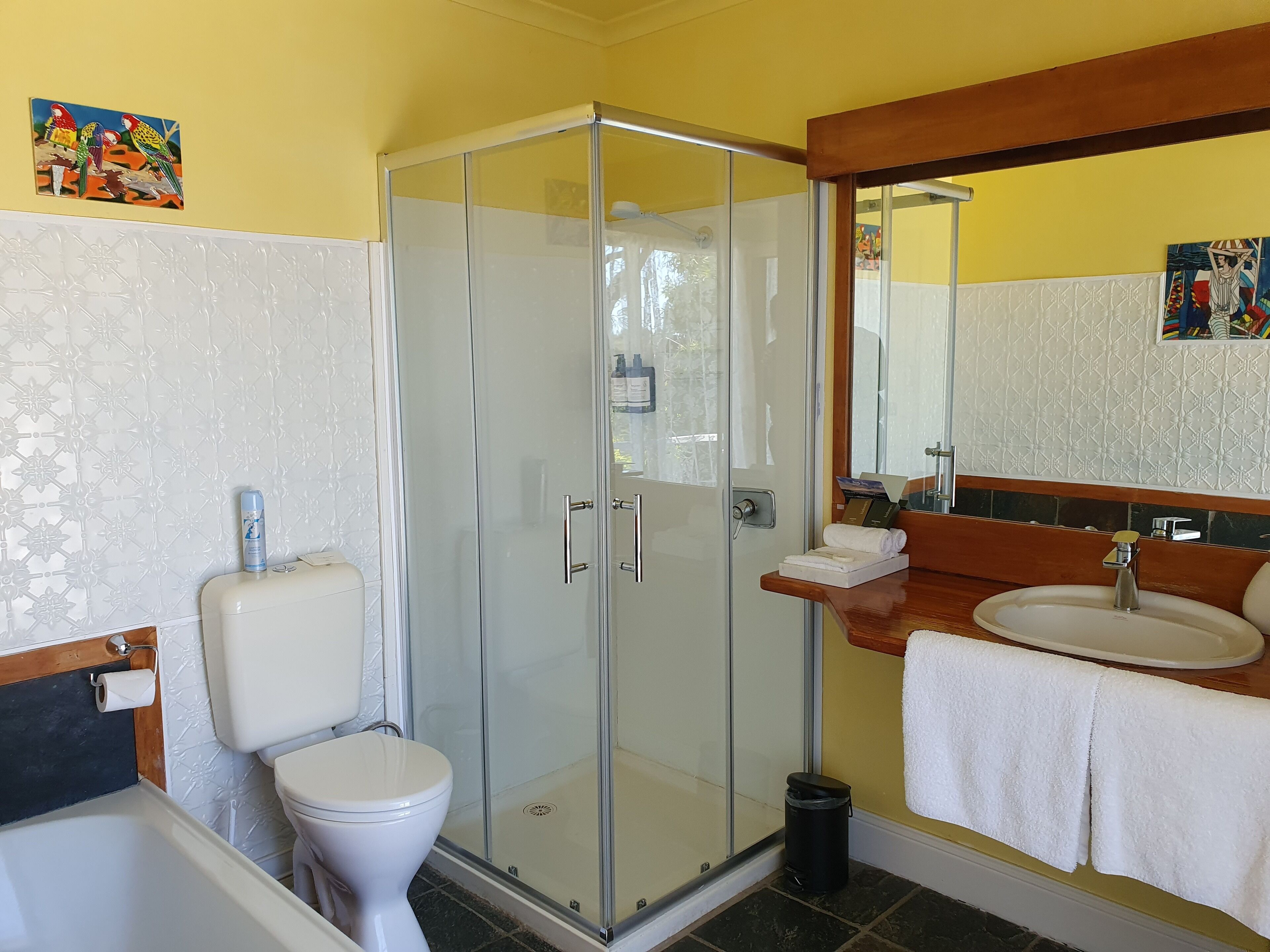 Un baño con ducha de mampara de vidrio, inodoro, lavamanos con espejo y decoración en las paredes.