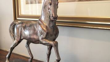 Une sculpture équestre en bronze, posée sur un socle en bois foncé, avec, en arrière-plan, un tableau encadré représentant des voiliers.