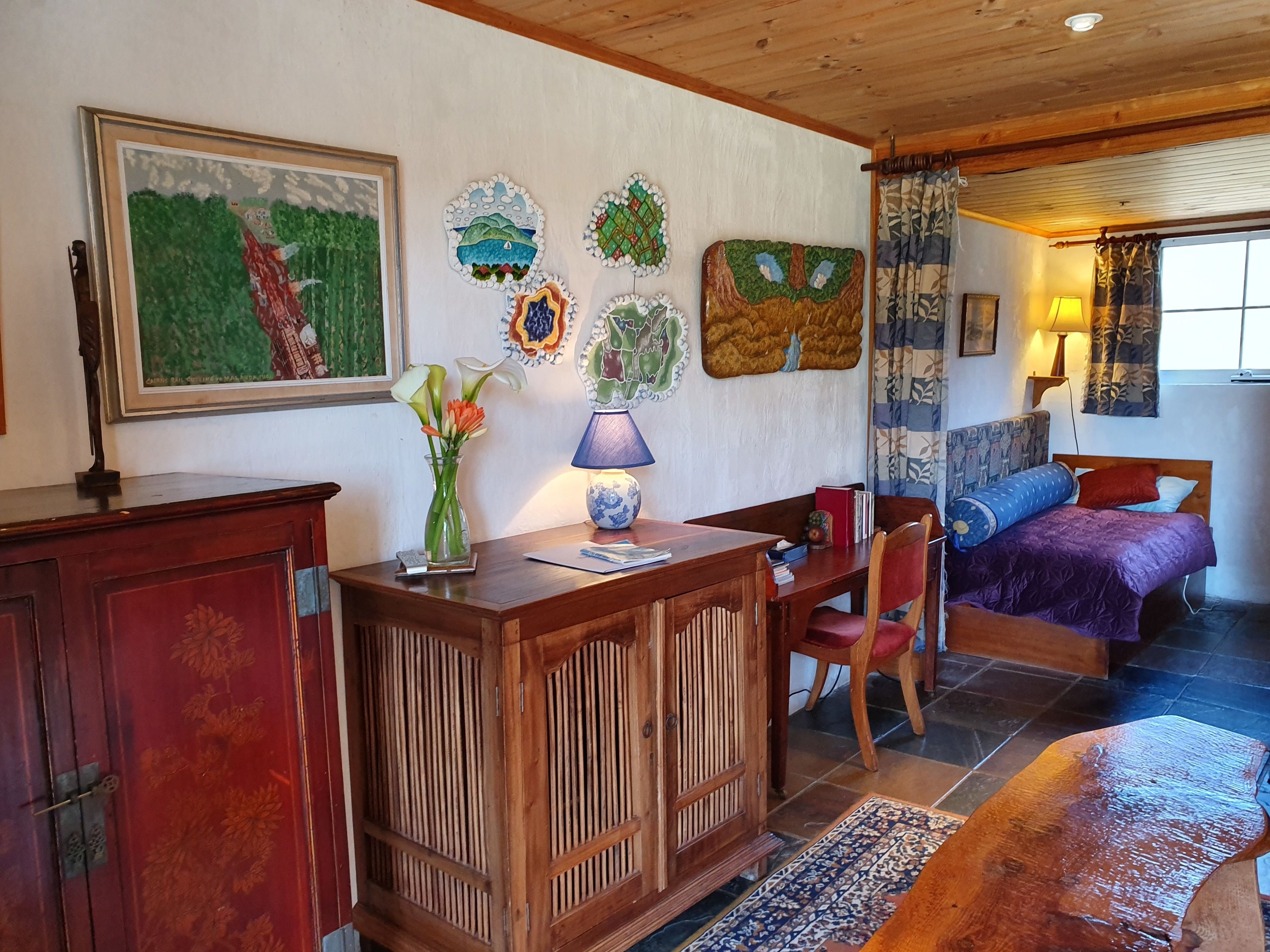 A cozy room with a bed, a desk, and a chair. There are decorative wall art pieces and a painting.