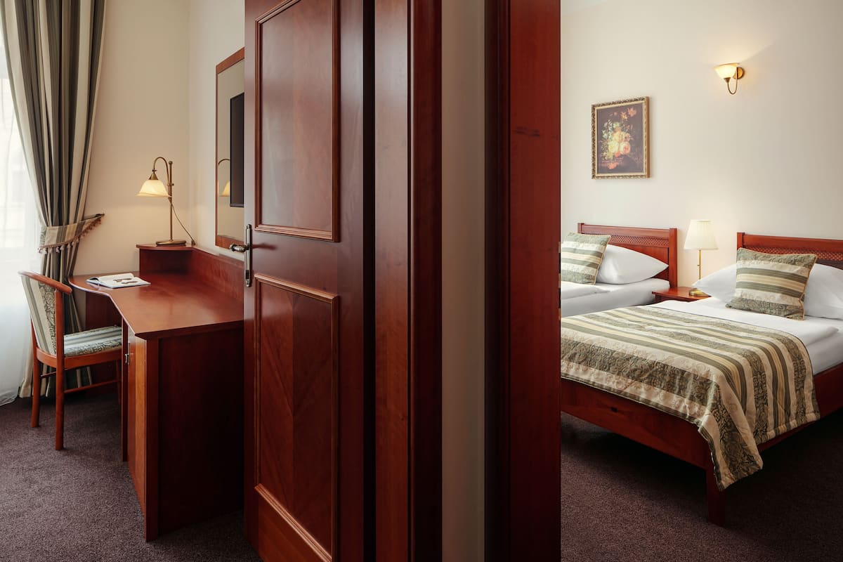 Een hotelkamer met een houten bureau, een stoel, een bed met een gestreept dekbed en een schilderij aan de muur.