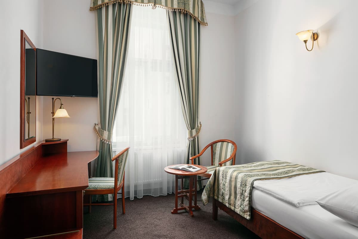 Hotelkamer met een bed, bureau, stoel, klein tafeltje, televisie en raam met gordijnen.