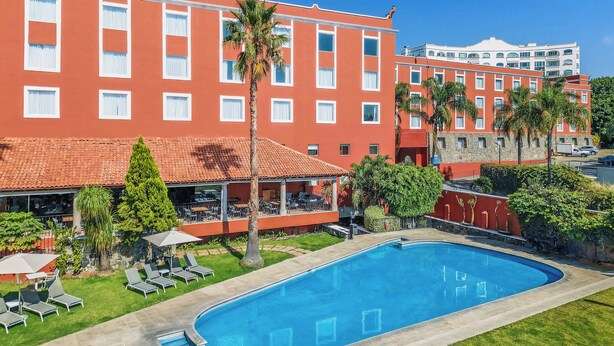 A hotel with a swimming pool, outdoor seating, and palm trees.